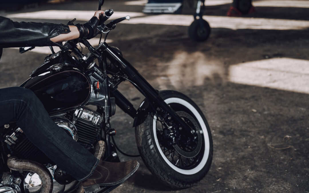 A close-up of a rider on a black ceramic-coated motorcycle with whitewall tires, parked in a shaded garage